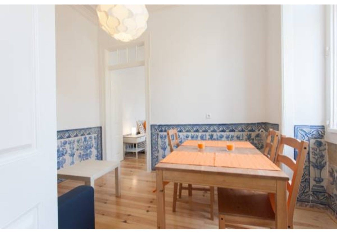 A dining area with a wooden table and chairs, a blue and white tiled backsplash, and a hanging light fixture.