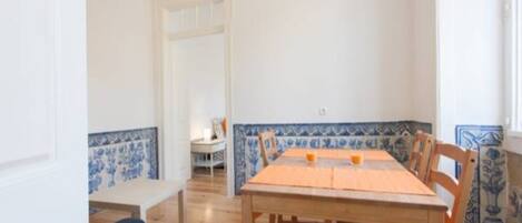 A dining area with a wooden table and chairs, a blue and white tiled backsplash, and a hanging light fixture.
