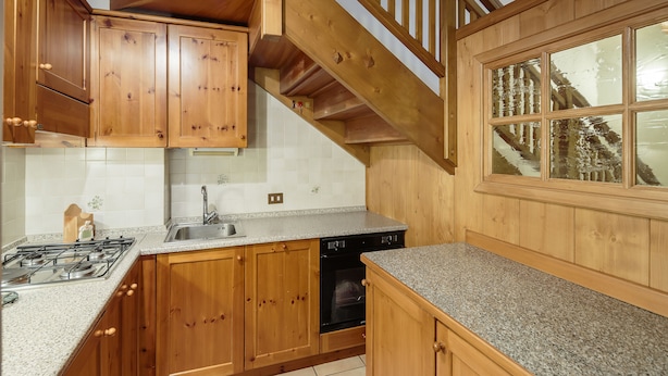 A kitchen with wooden cabinets, a granite countertop, a dishwasher, and a stove. - Villa Lacedel (Cortina d'Ampezzo)