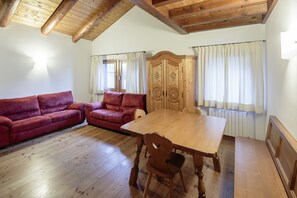 Ein Zimmer mit einem Holzespeisetisch, zwei Holzstühlen, einem Holzschrank und zwei roten Sofas.
