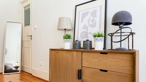 A wooden cabinet with drawers, a mirror, a framed abstract artwork, a lamp, and decorative pots with plants. - Gonzalo's Guest Apartments - Downtown Historic Flats I (Lisbon)