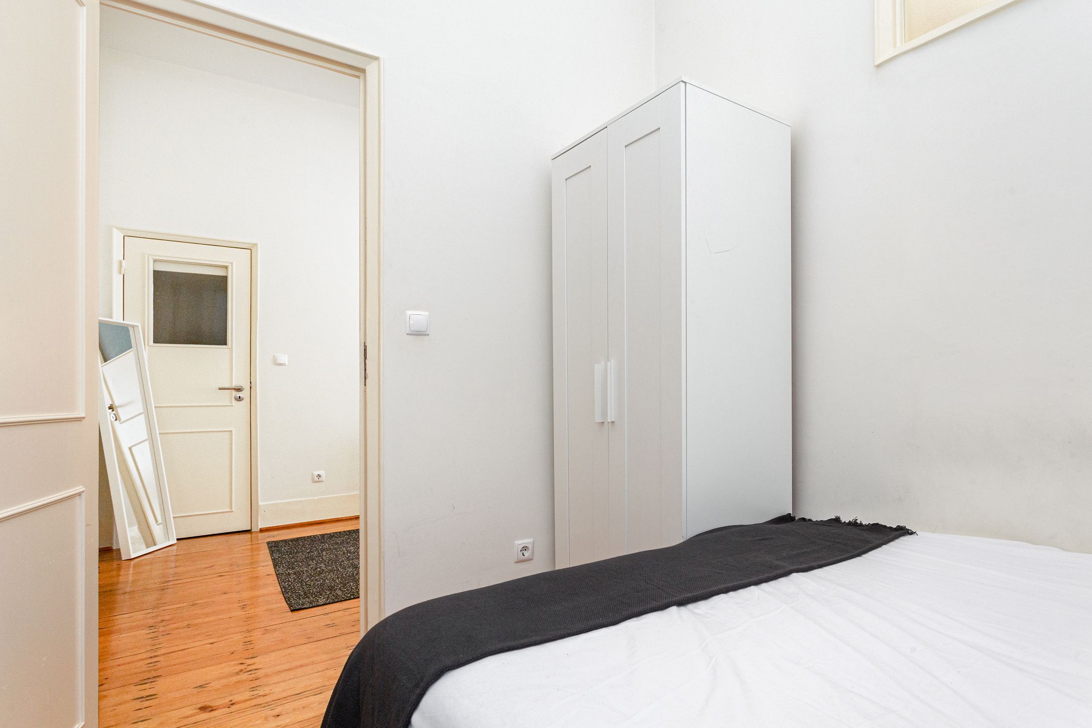 A bedroom with a bed, a wardrobe, and a door leading to another room.
