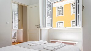 A hotel room with a bed, a chair, a window, and a view of a yellow building. - Gonzalo's Guest Apartments - Downtown Historic Flats I (Lisbon)
