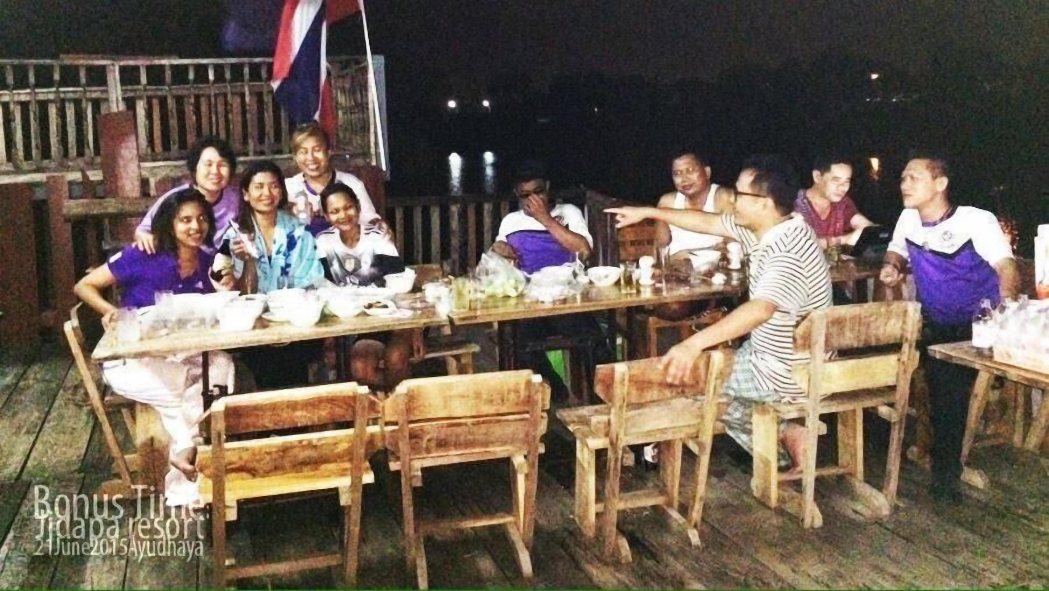 A group of people seated around a wooden table with various dishes, likely enjoying a meal outdoors at a resort.