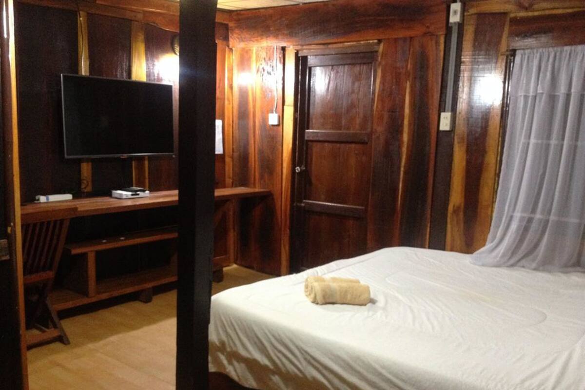 A wooden room with a bed, a television on a wooden stand, and a door.