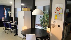 A modern office space with a round table, chairs, a refrigerator, a lamp, and a bulletin board with notes. - Alternative Creative Youth Hostel Barcelona (Barcelona)