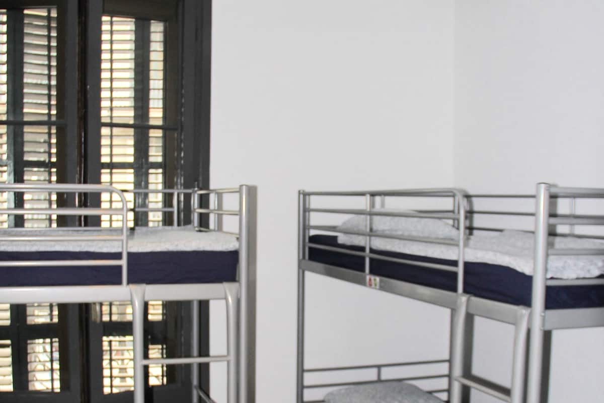 Um quarto de dormitório com beliches, uma janela com persianas e piso de azulejos.
