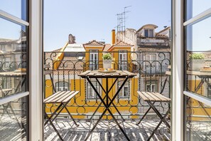 Een balkon met een houten tafel en stoelen, een bloempot en uitzicht op gele gebouwen met balkons.