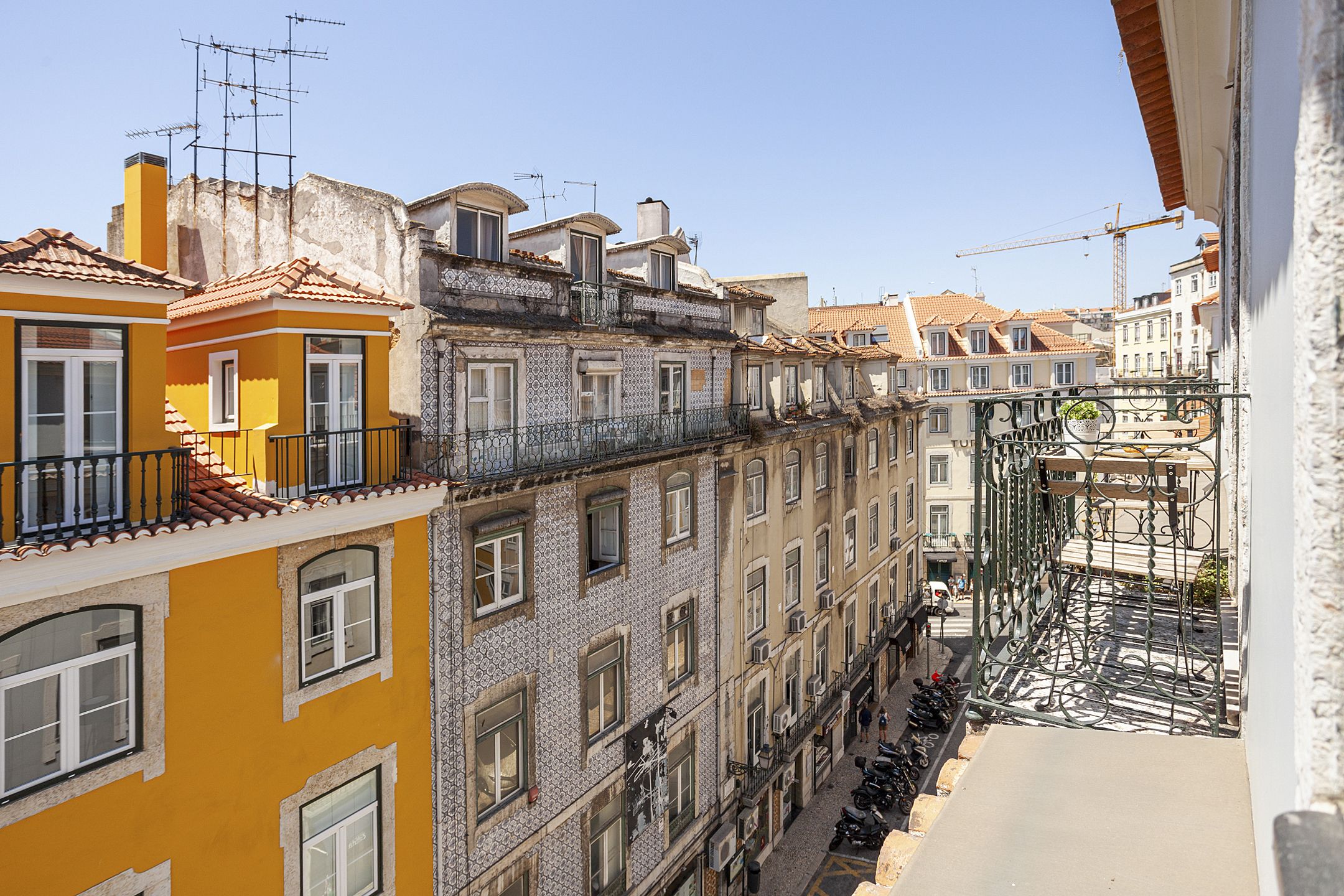 A narrow street with buildings on both sides, featuring balconies and a construction crane in the background.