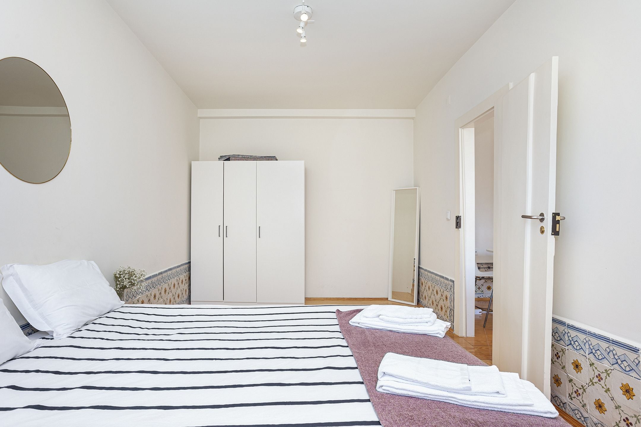 A bedroom with a bed, a wardrobe, a mirror, and a bathroom visible through an open door.