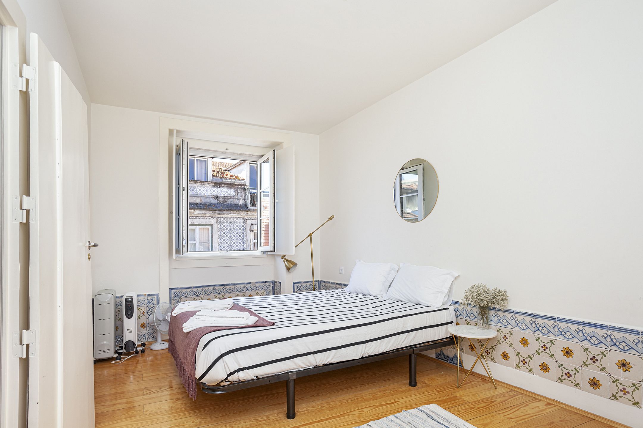 Een slaapkamer met een bed, nachtkastje, spiegel, raam en radiator.