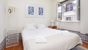 A hotel room with a neatly made bed, a white wardrobe, and a window with a view of a building. - Gonzalo's Guest Apartments - Downtown Historic Flats III (Lisbon)