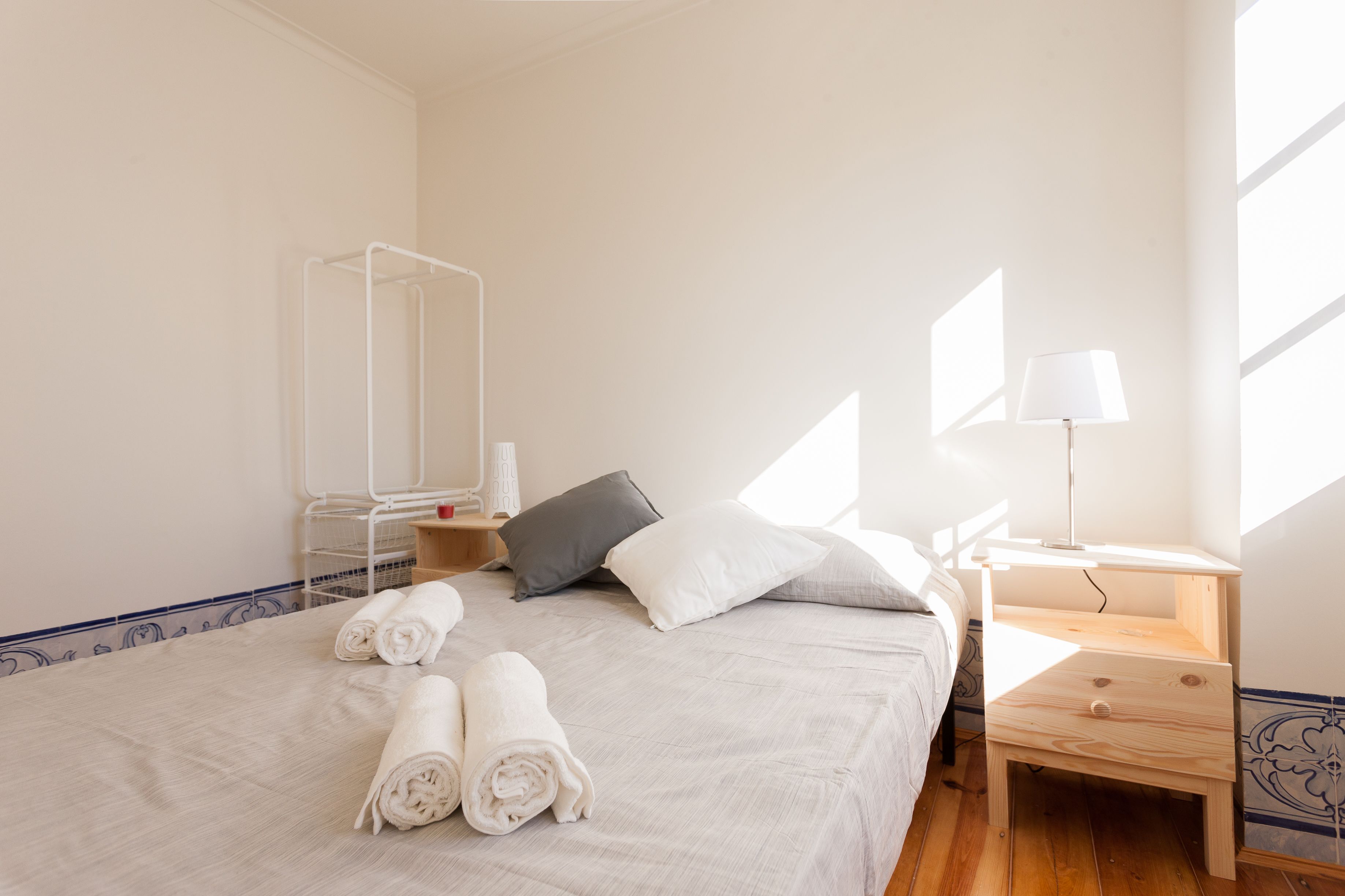 A neatly made bed with rolled towels, a bedside table with a lamp, and a mirror on the wall.