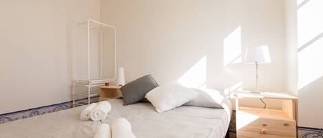 A neatly made bed with rolled towels, a bedside table with a lamp, and a mirror on the wall.