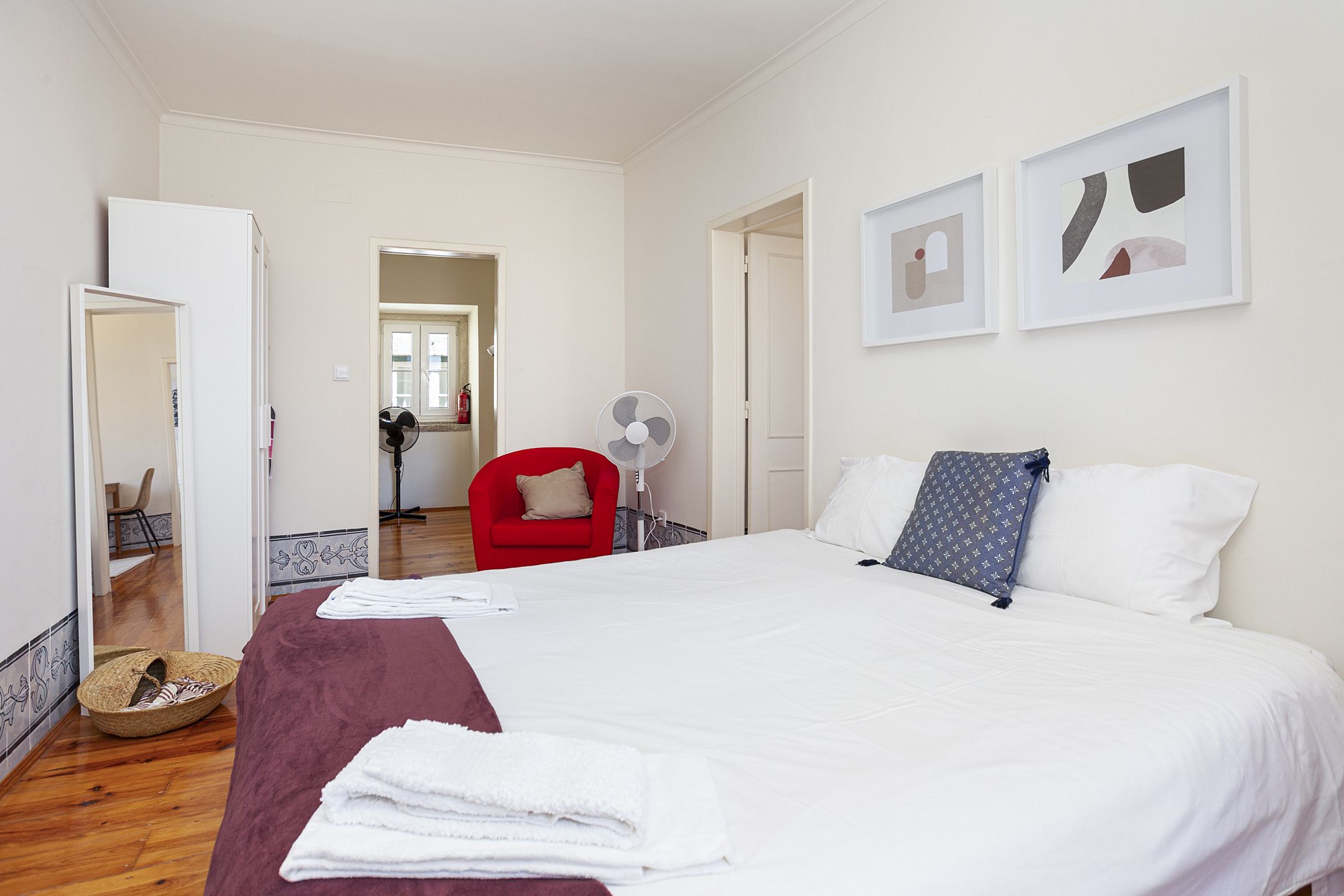Una habitación de hotel con una cama grande, una silla roja y dos cuadros en la pared.