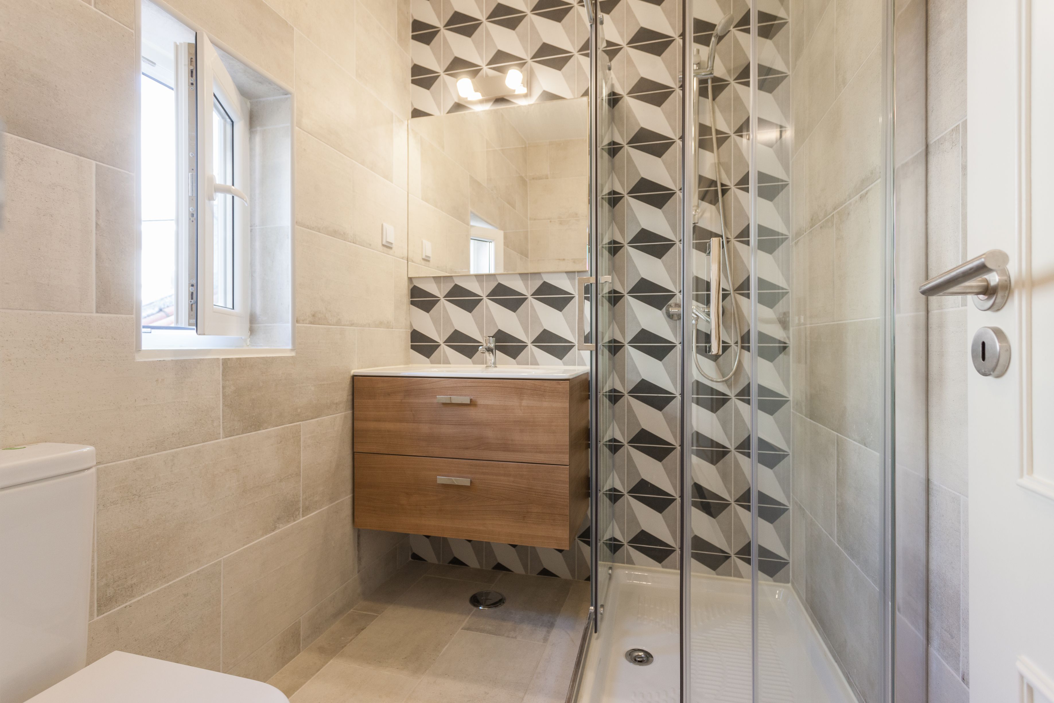 A modern bathroom with a glass shower enclosure, a wooden vanity, and a geometric tile backsplash.