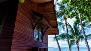 A wooden building with a balcony overlooking a beach with palm trees and a body of water. - Bangrak Pier Bungalow (Koh Samui)