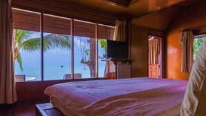 A bedroom with a large bed, a TV on a wooden stand, and a view of the ocean through large windows. - Bangrak Pier Bungalow (Koh Samui)