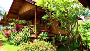 A wooden structure with a covered porch, surrounded by lush greenery and flowering plants. - Bangrak Pier Bungalow (Koh Samui)