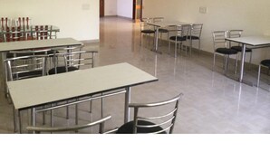 Una habitación amplia con varias mesas y sillas, un ventilador de techo y una puerta que da a otra zona.