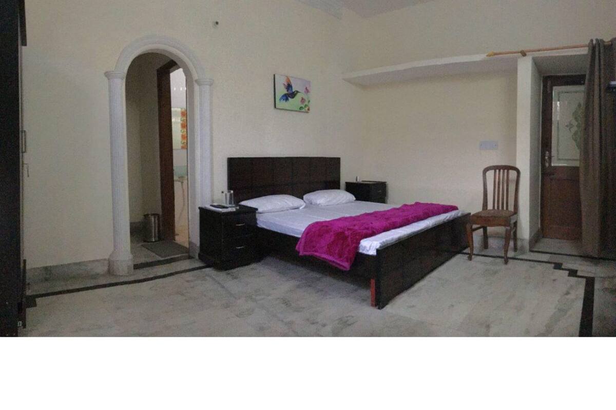Een slaapkamer met een bed, nachtkastje, stoel en een boogvormige deuropening.