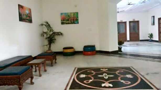 Una habitación amplia con ventilador de techo, dos cuadros en las paredes, piso estampado y un espacio de descanso con sofá y sillones.