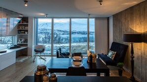 Ett modernt vardagsrum med ett stort fönster som vetter mot ett snötäckt landskap, en matplats med ett bord dukat för två personer och en mysig sittgrupp med en lampa.