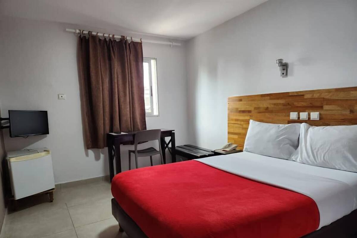 A hotel room with a bed, a desk, a chair, a television, and a window with curtains.