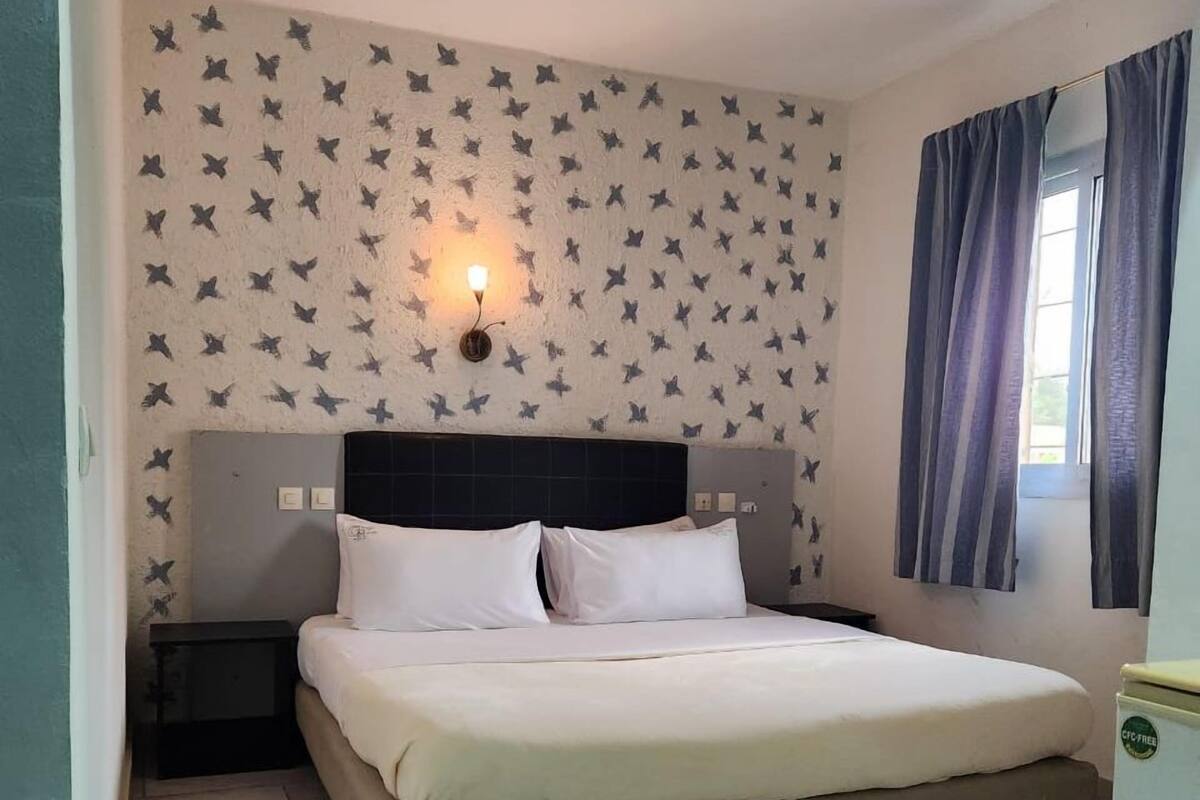 A bedroom with a bed, a nightstand, and a wall-mounted light fixture.