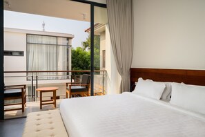 Ein Hotelzimmer mit einem großen Bett, einem Balkon mit Tisch und Stühlen sowie Blick auf Grünflächen und Gebäude.