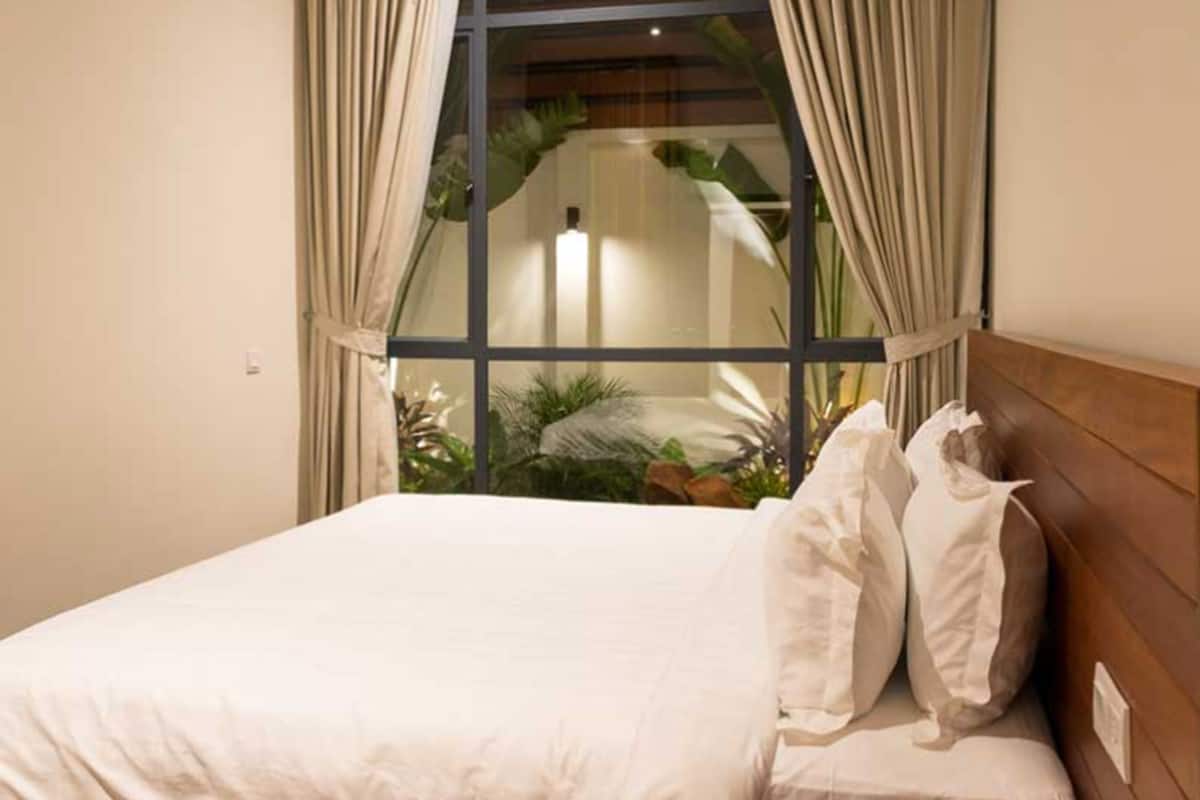 A neatly made bed with white linens and a wooden headboard in a room with a large window.