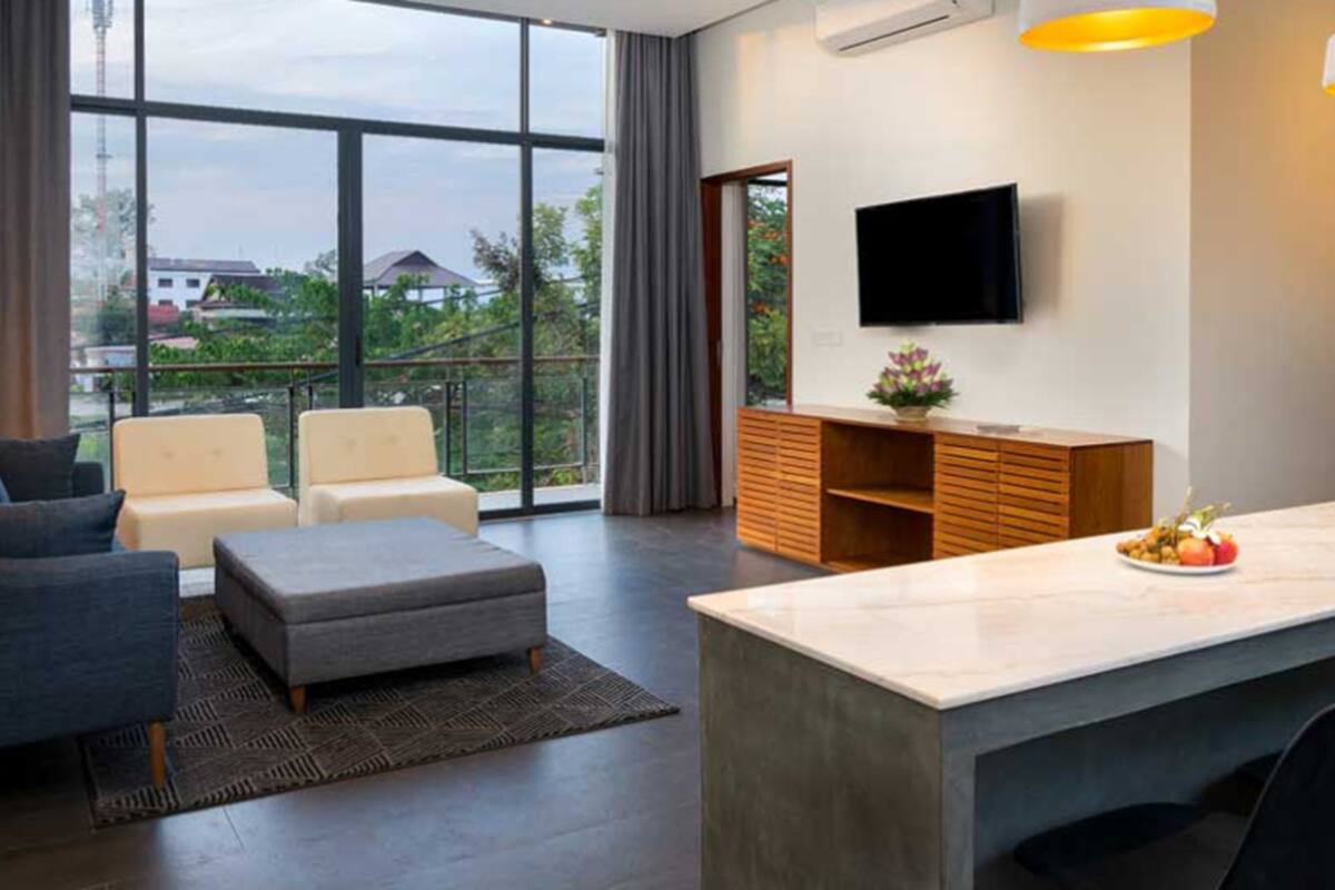 A modern living room with a sofa, a grey ottoman, a wooden cabinet, and a TV mounted on the wall.