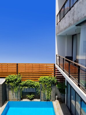 A rooftop pool area with a wooden deck, potted plants, and a glass balustrade.