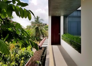 Enter a tranquil oasis, surrounded by lush greenery and a palm tree, with a serene water feature and a pathway leading to a secluded entrance.
