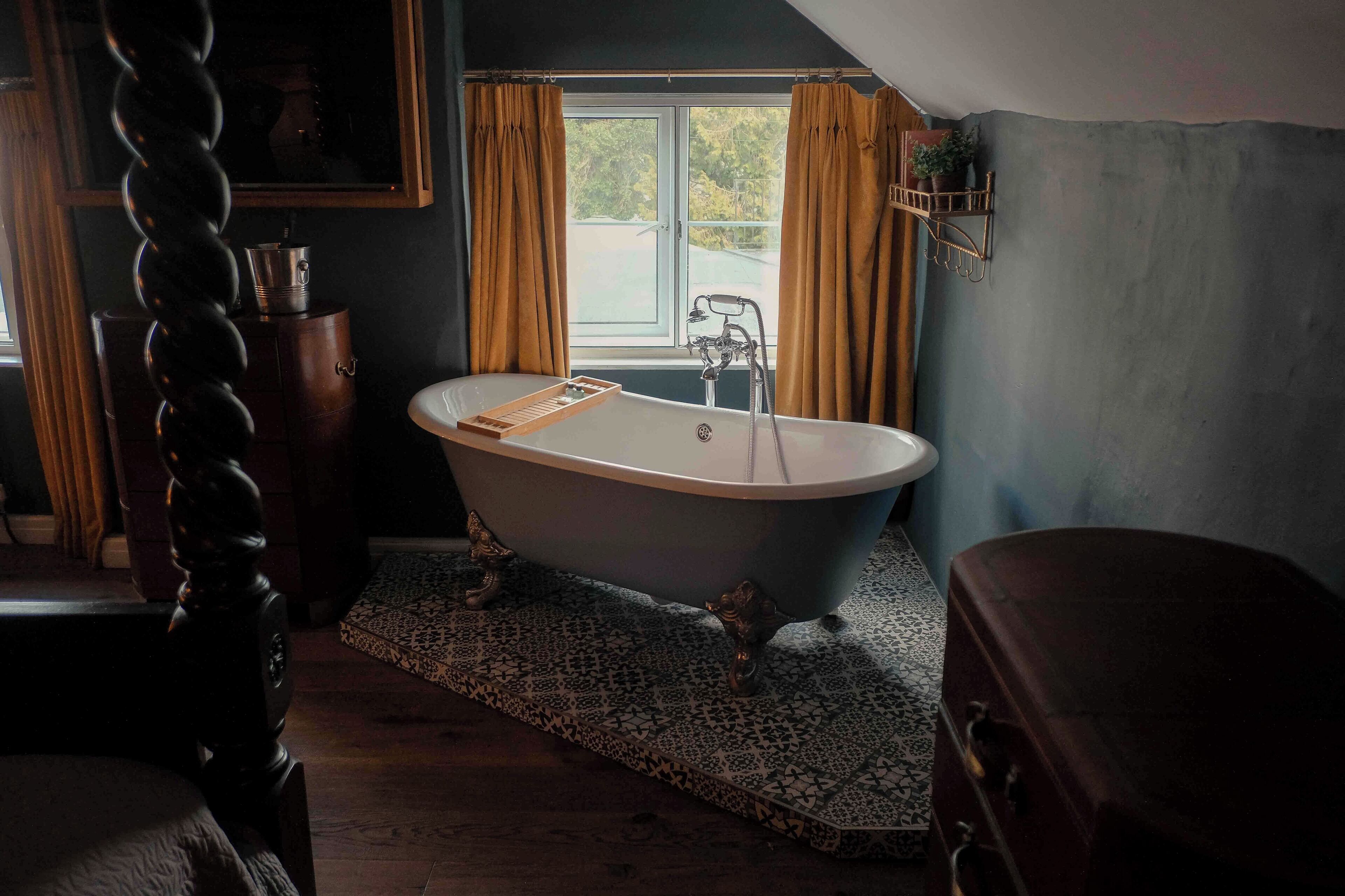 Ein Badezimmer mit einer freistehenden Badewanne, einem Holzkabinett, einem gemusterten Teppich und einem Fenster mit Vorhängen.