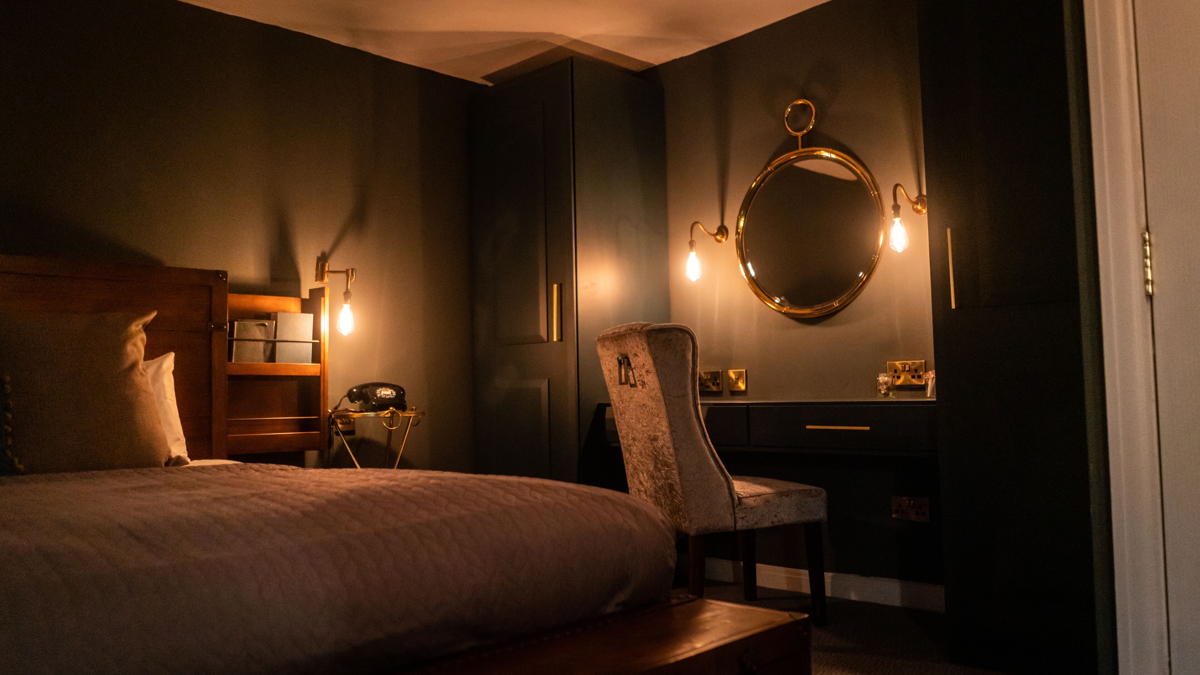 A bedroom with a bed, a desk, a chair, a dresser, and a mirror.