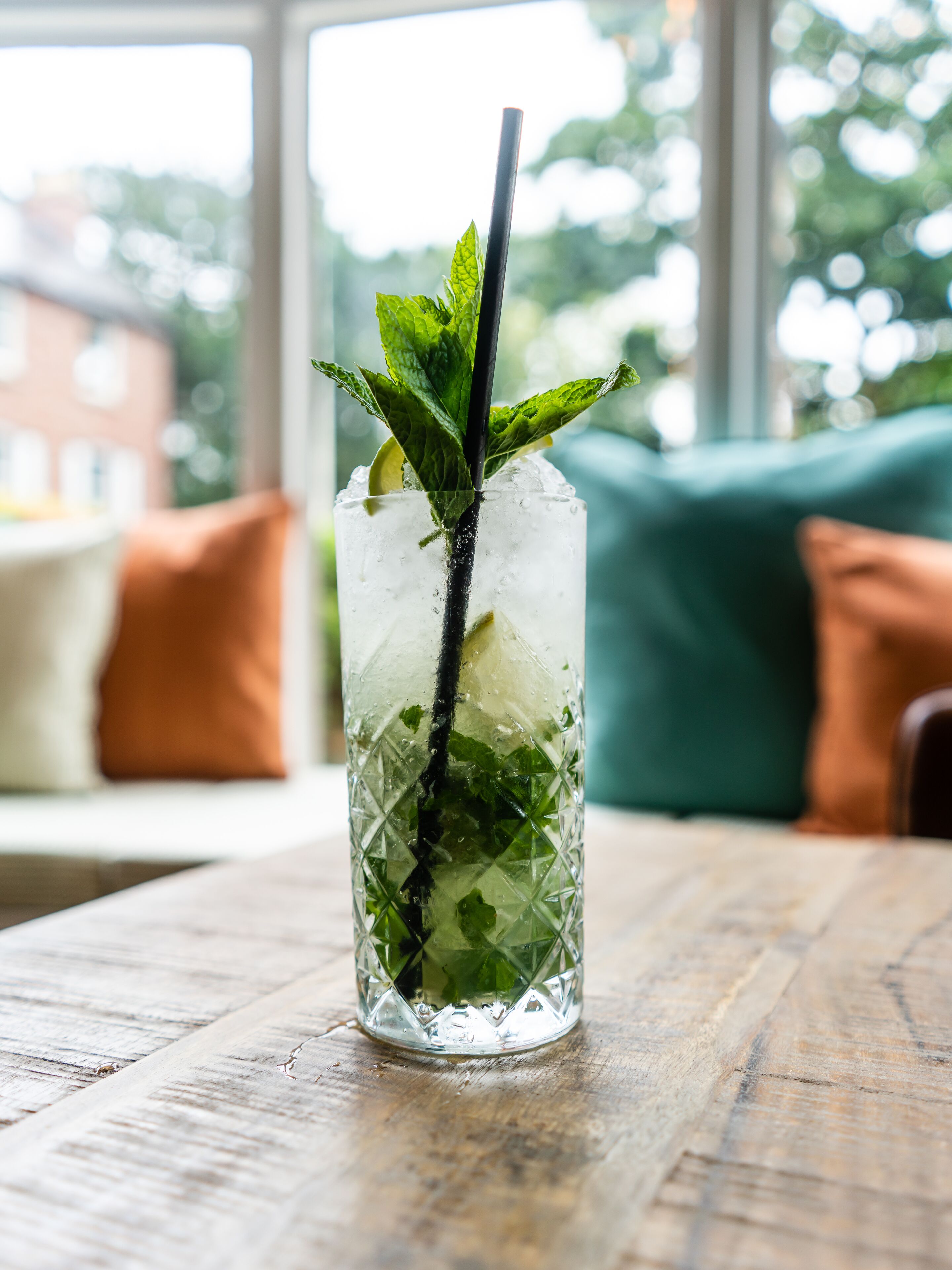 A clear glass with ice cubes, mint leaves, and a straw on a wooden table.