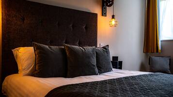 Ein ordentlich bezogenes Bett mit dunklem Kopfteil, mehreren Kissen und einer gesteppten Decke.