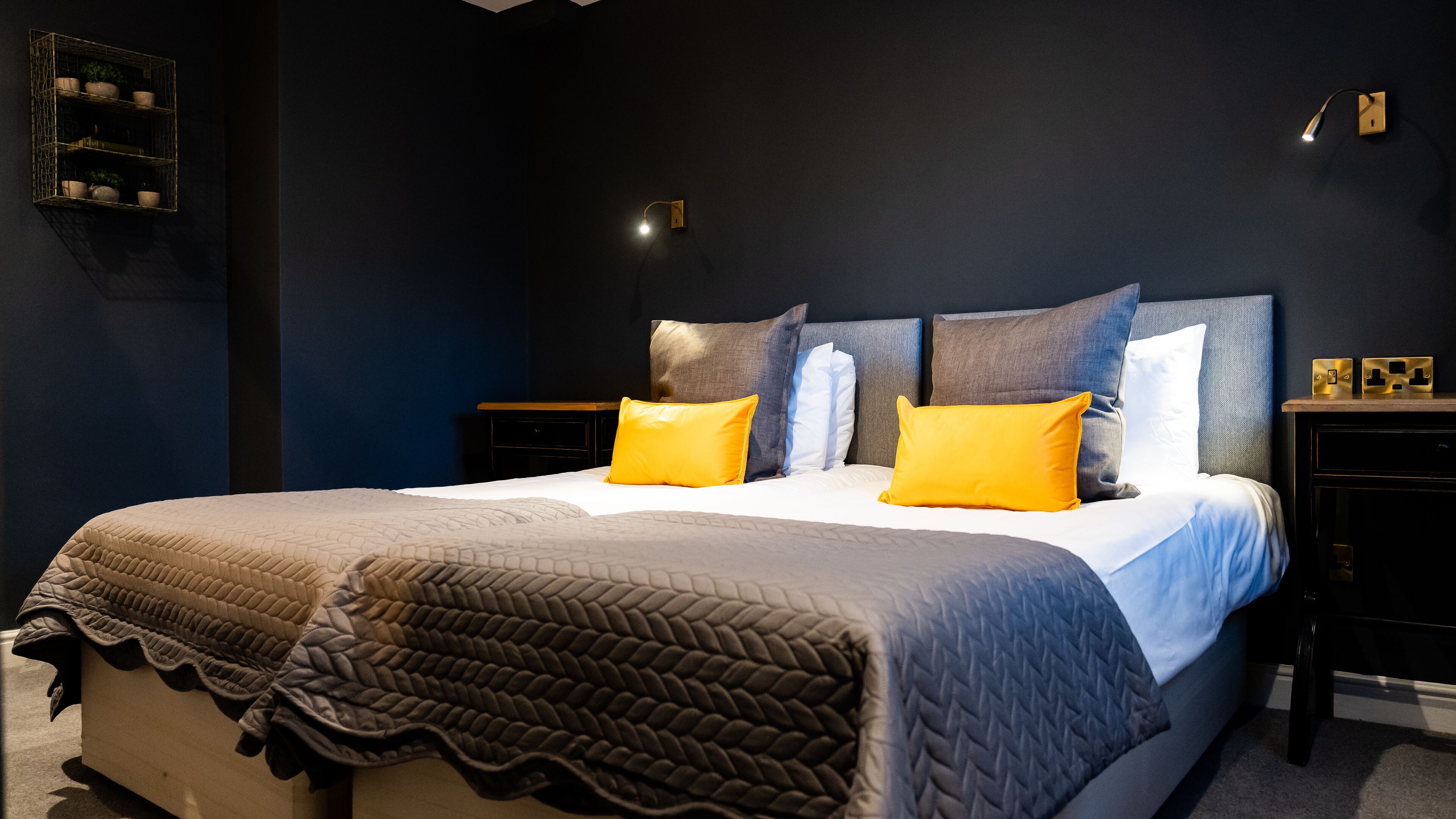 A neatly made bed with a grey quilt, two yellow pillows, and a dark blue headboard.
