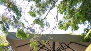 An outdoor patio area with tables and chairs under a large umbrella, surrounded by greenery and stone steps. - The Bridge (Macclesfield)