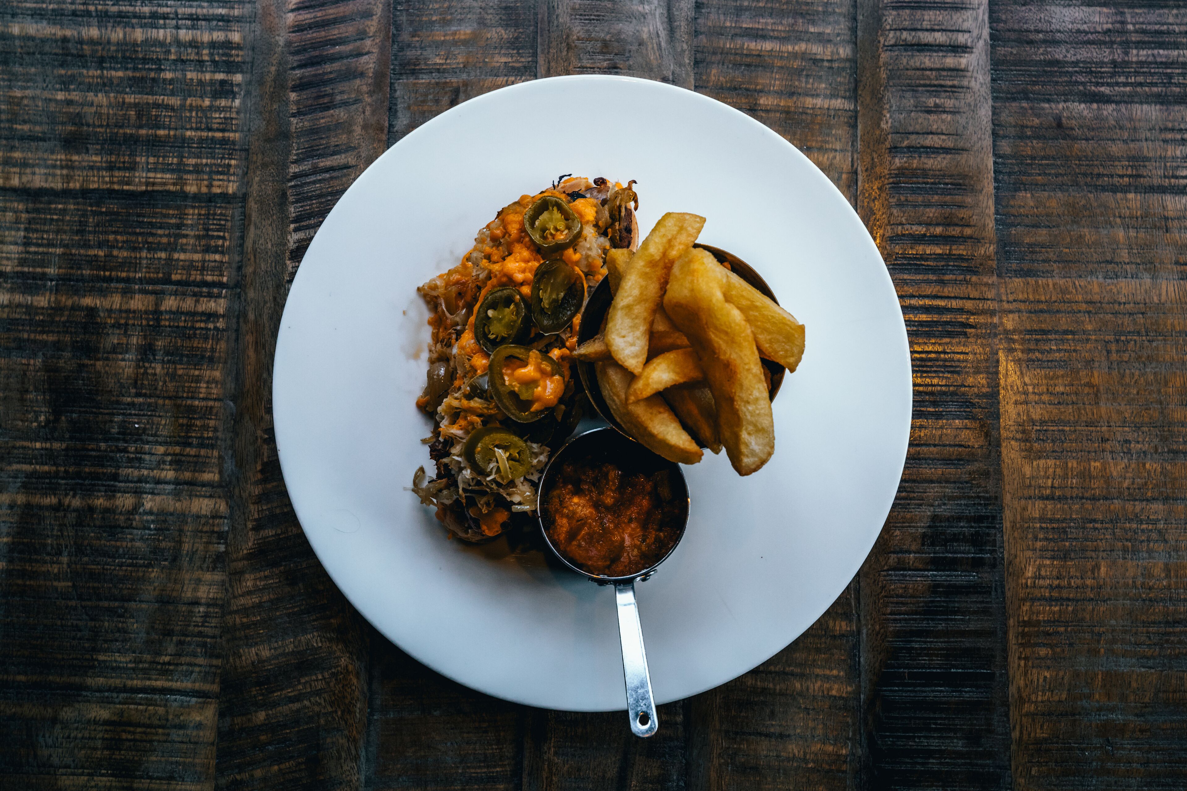 A plate of food with a small bowl of sauce and fries on a wooden table.
