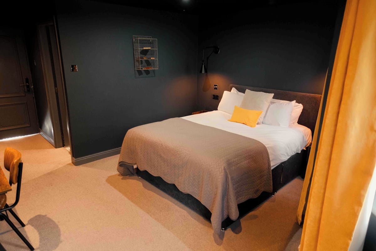 A bedroom with a bed, a chair, a nightstand, and a wall-mounted light fixture.
