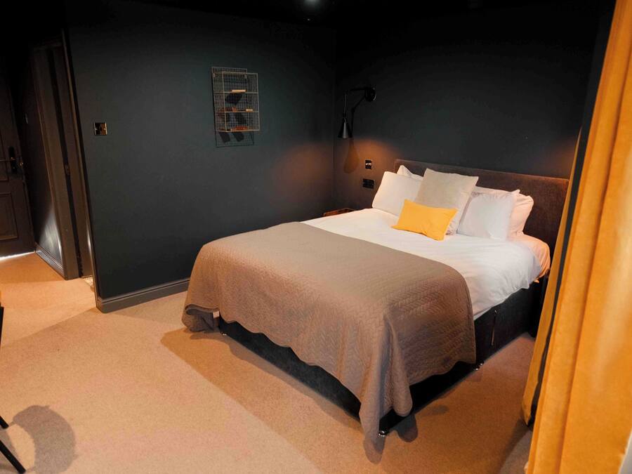 Ein Schlafzimmer mit einem Bett, einem Sessel, einem Nachttisch und einer Wandleuchte.
