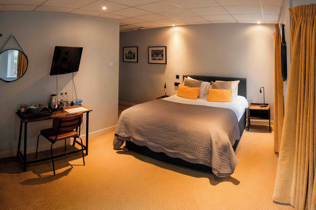 A hotel room with a bed, a desk, a chair, a TV, and a nightstand.