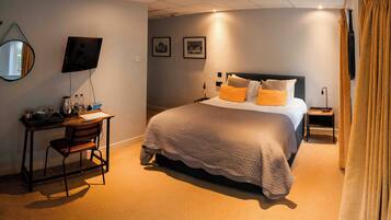 Una habitación de hotel con cama, escritorio, silla, televisión y mesita de noche.