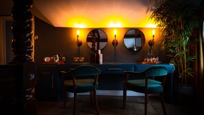 A bar area with a dark blue counter, two green upholstered chairs, and three wall-mounted mirrors. - The Bridge (Macclesfield)