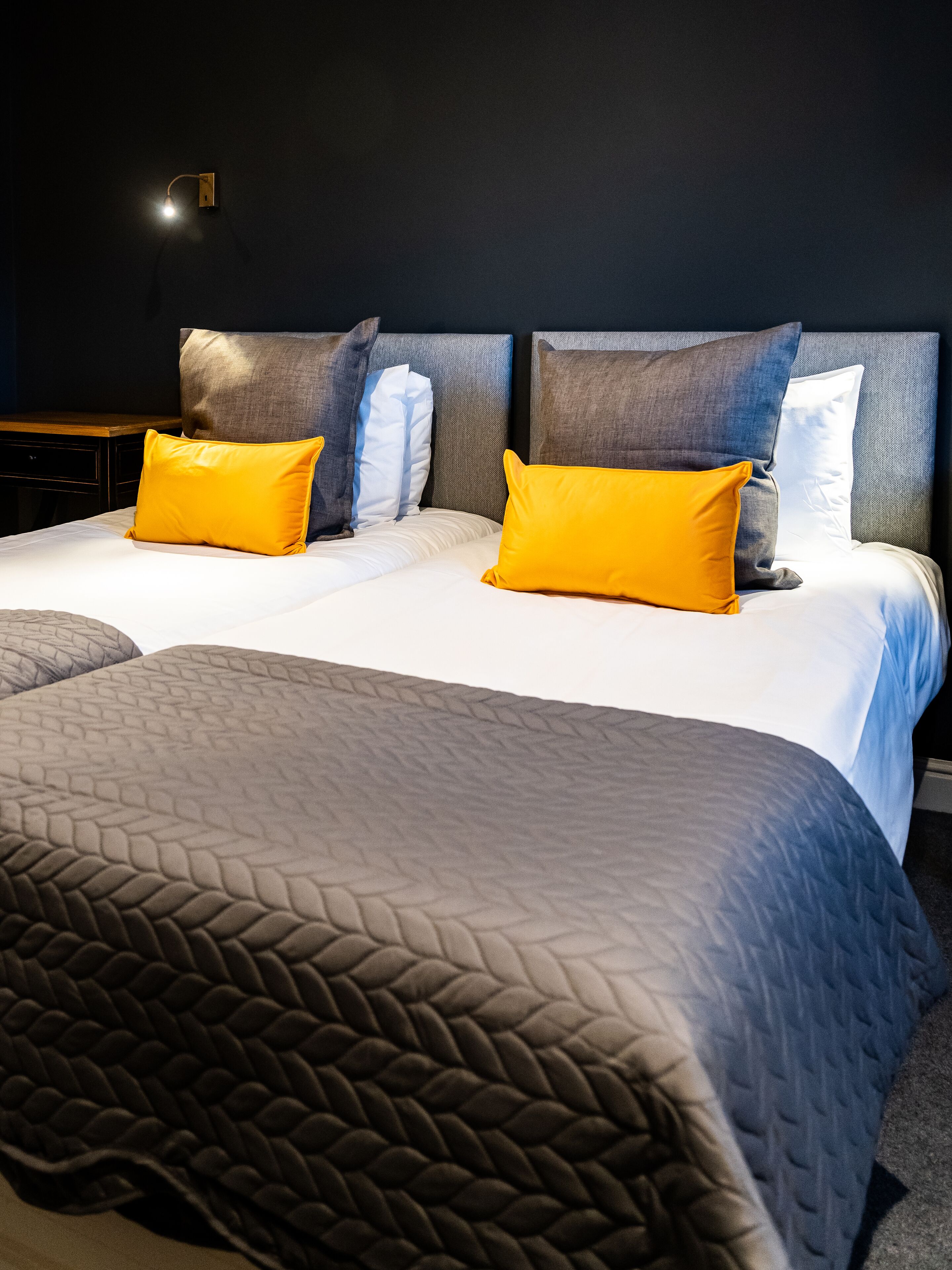 Una cama doble con una colcha acolchada gris, dos almohadas amarillas y un cabecero gris.