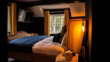 A hotel room with a bed, a bedside table with a lamp, a TV mounted on the wall, and a window with curtains.