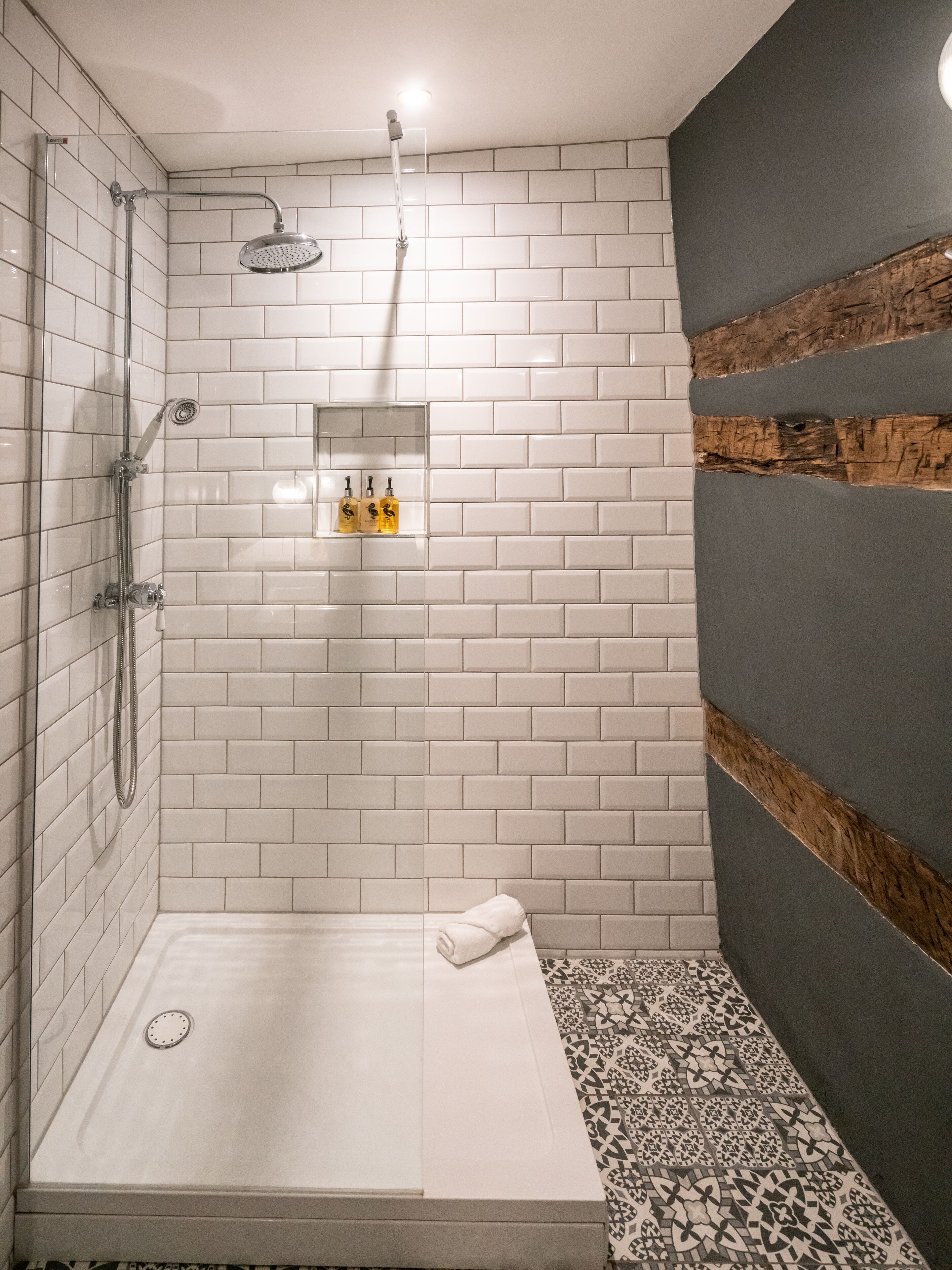 Un área de ducha moderna con azulejos blancos, puerta de vidrio y una pared de acento de madera.