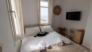 Een hotelkamer met een bed, een televisie, een klein houten kastje en uitzicht op het strand.